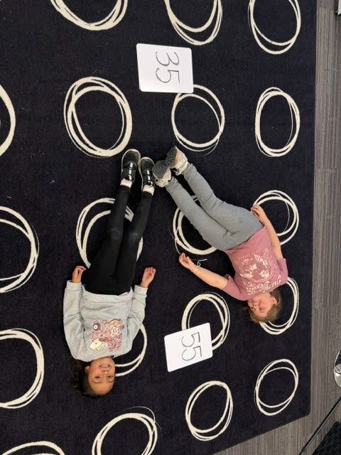 Students creating math greater than, less than or equal value signs with their bodies on the floor