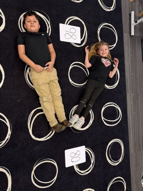 Students creating math greater than, less than or equal value signs with their bodies on the floor