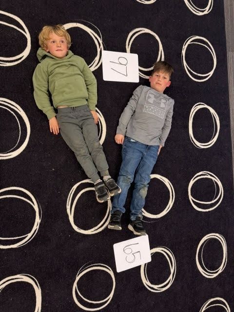 Students creating math greater than, less than or equal value signs with their bodies on the floor