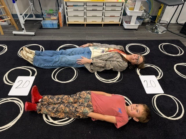 Students creating math greater than, less than or equal value signs with their bodies on the floor