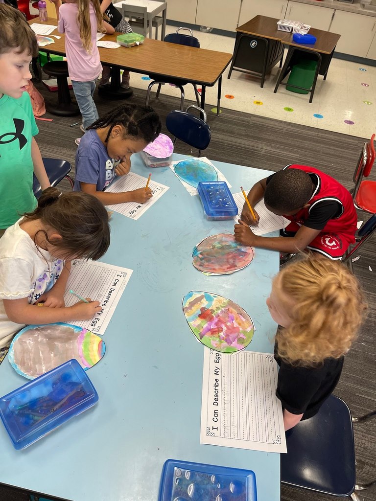 students paint an easter egg with watercolor paints and practicing descriptive writing on space provided under the egg on the paper.