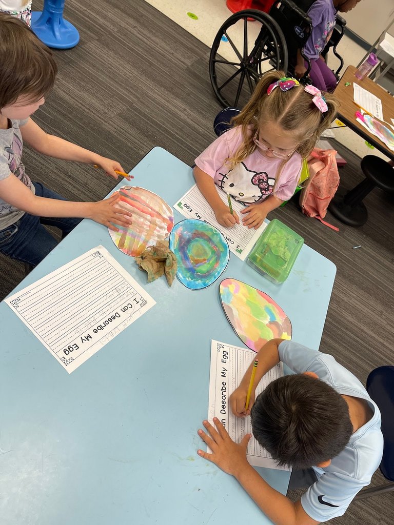 students paint an easter egg with watercolor paints and practicing descriptive writing on space provided under the egg on the paper.