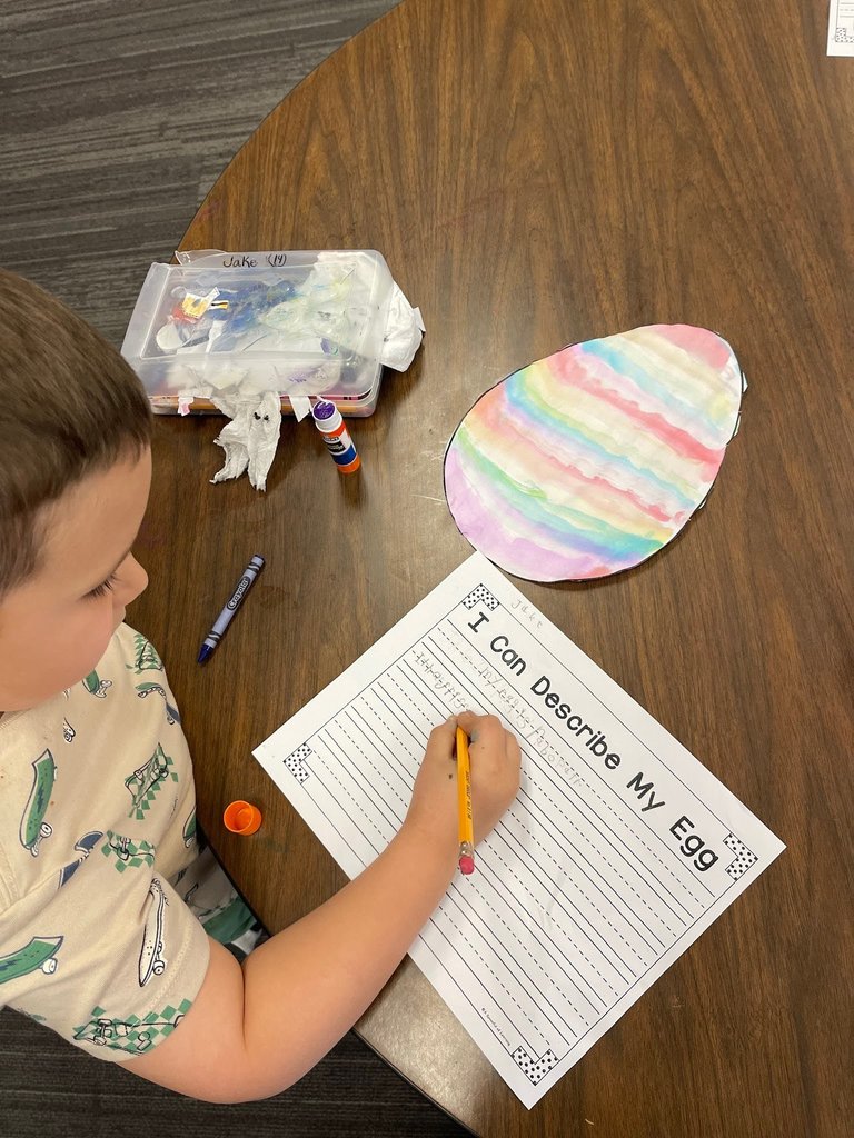 students paint an easter egg with watercolor paints and practicing descriptive writing on space provided under the egg on the paper.