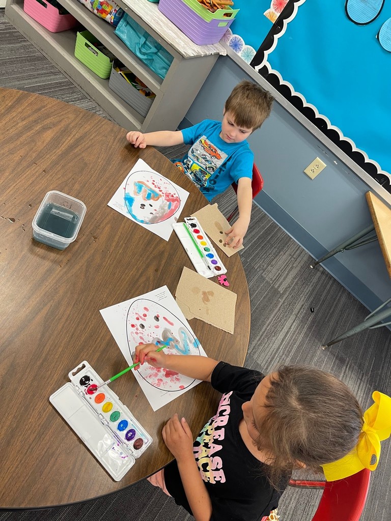 students paint an easter egg with watercolor paints and practicing descriptive writing on space provided under the egg on the paper.