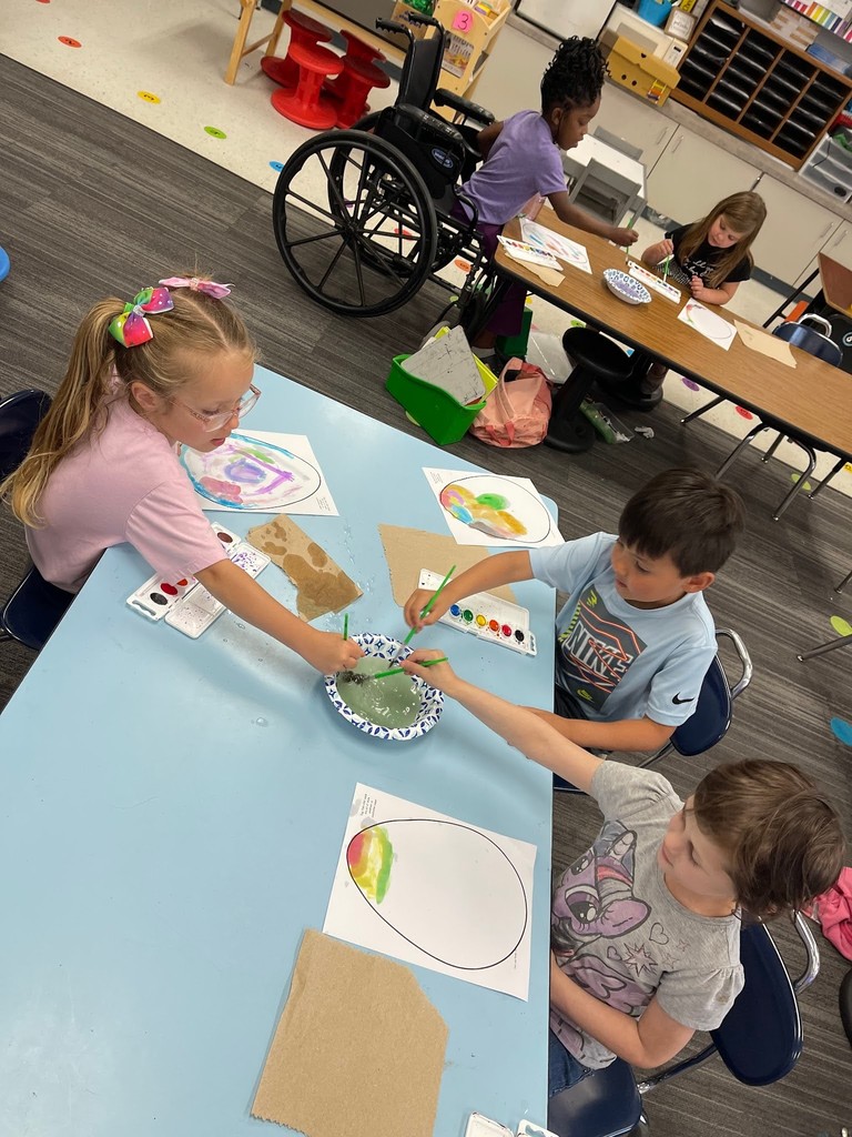 students paint an easter egg with watercolor paints and practicing descriptive writing on space provided under the egg on the paper.
