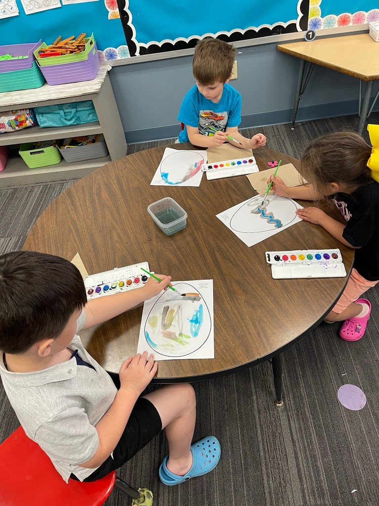 students paint an easter egg with watercolor paints and practicing descriptive writing on space provided under the egg on the paper.