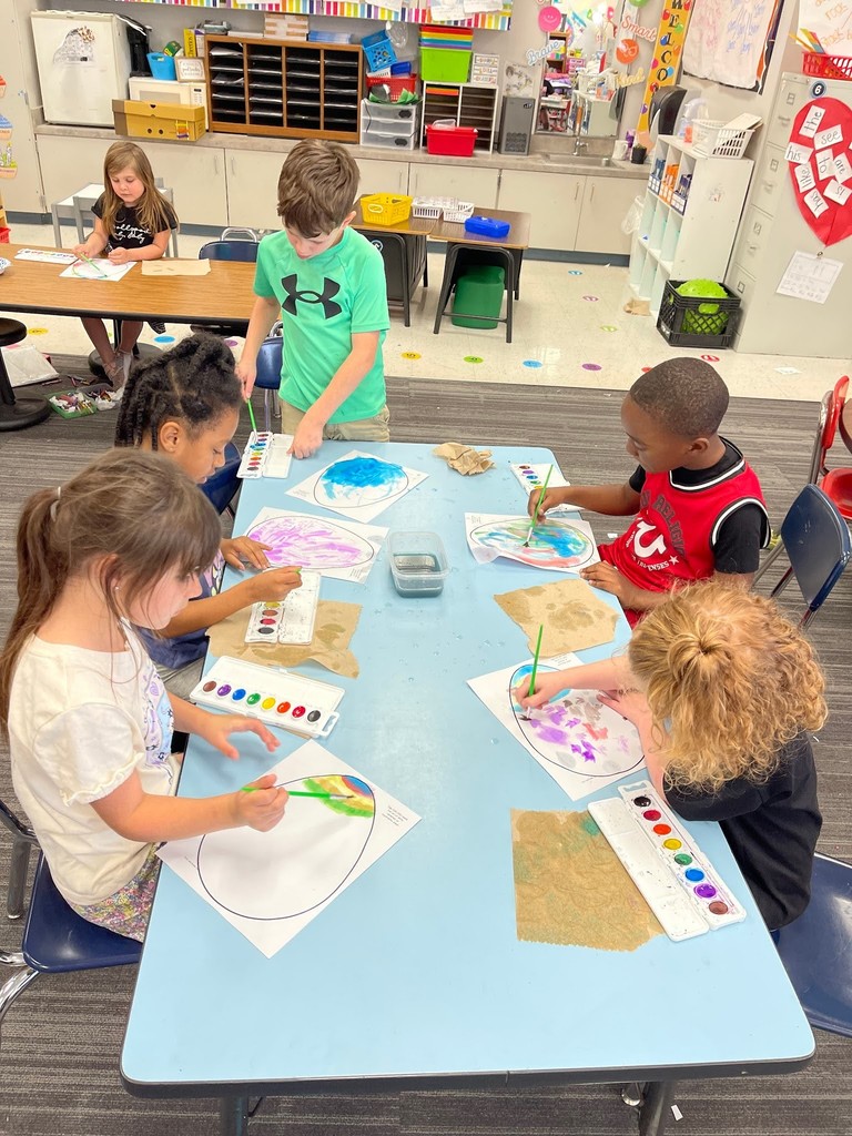 students paint an easter egg with watercolor paints and practicing descriptive writing on space provided under the egg on the paper.