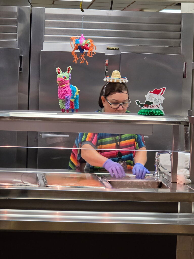 A person in a kitchen wearing gloves, standing at a table with a display case in front.