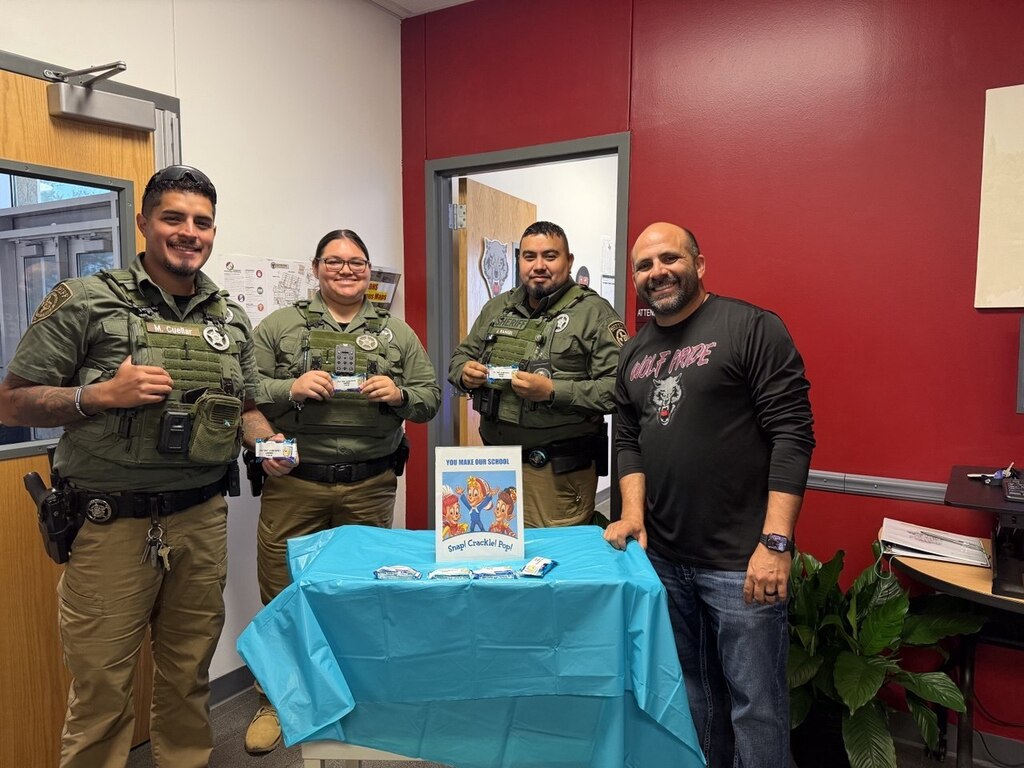 Four individuals in uniform stand beside a table with a tablecloth. One holds a book.