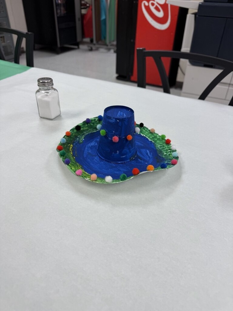 A white table displays a blue sombrero with colorful pom-poms and a small salt shaker.