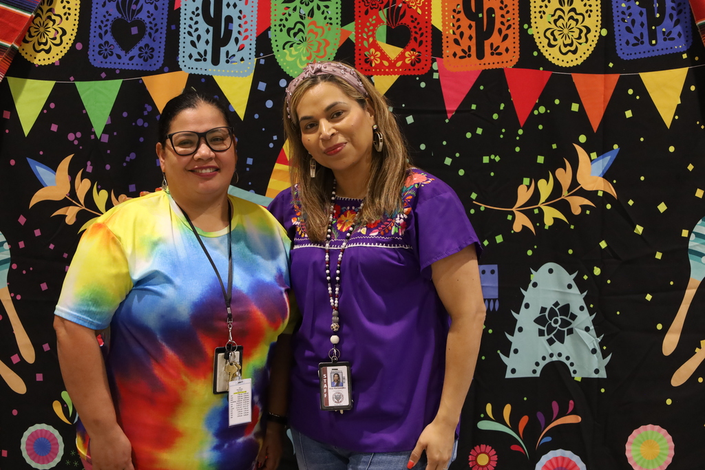 Two women stand next to each other in front of a colorful backdrop with patterns.