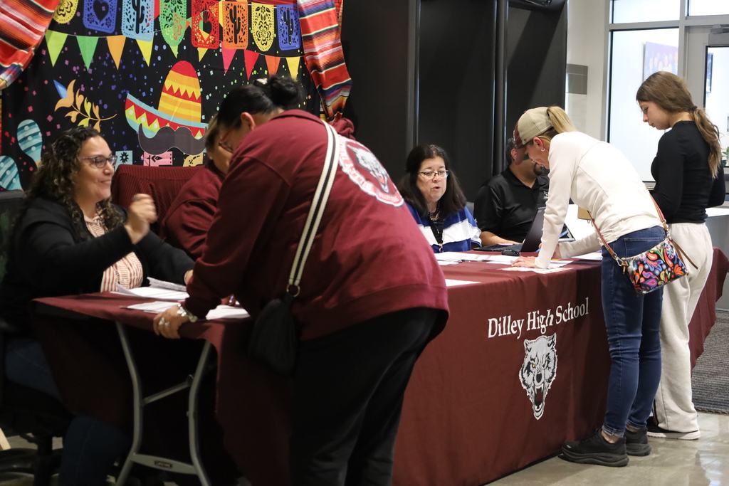 People seated at a desk with a table cloth, and others standing behind the desk, signing papers.