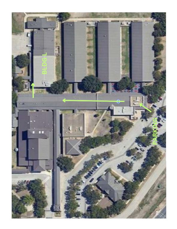 Overhead view of a building complex. Multiple rectangular buildings and a parking area. Green lines indicate directions.