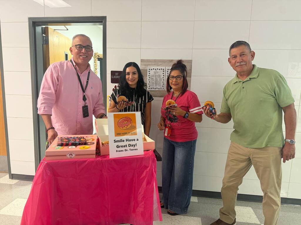 Four people pose by a table with food. A sign reads "Double Meat Burrito" and "Bread & Beans".