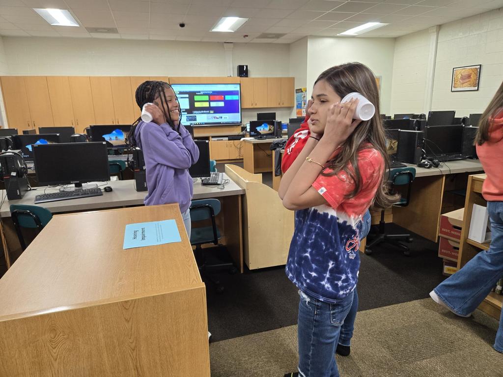 Students use cups to impair their hearing to simulate having a hearing impairment.