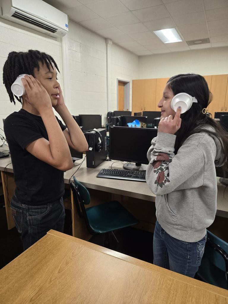 Students use cups to impair their hearing to simulate having a hearing impairment.