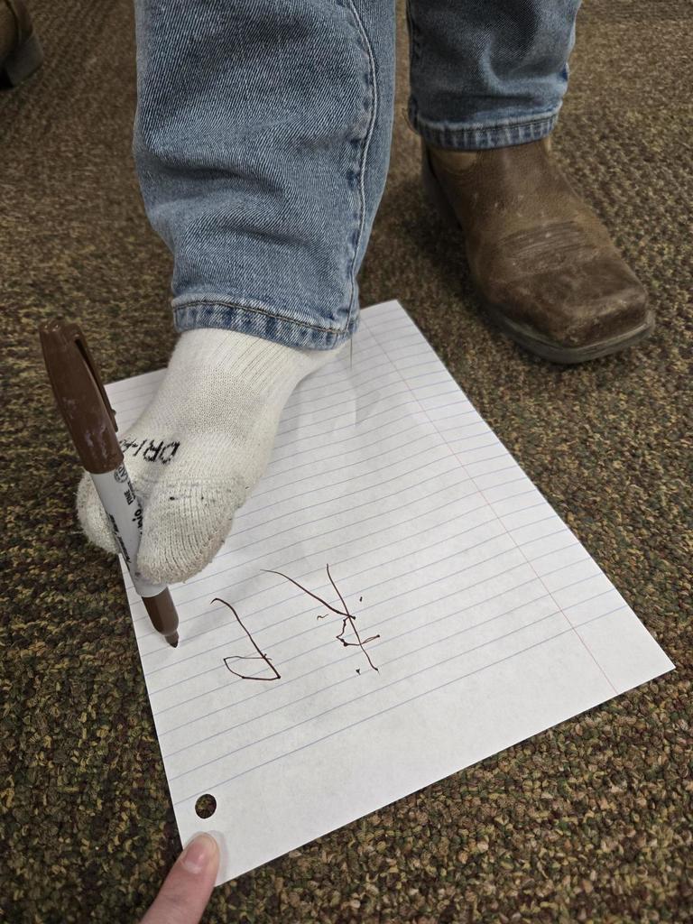 Student attempts to write his name with his foot.