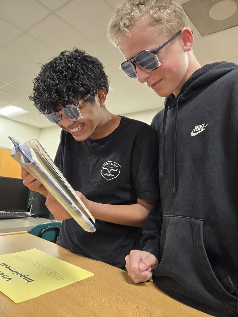 Students attempt to read while wearing visual impairment sunglasses.