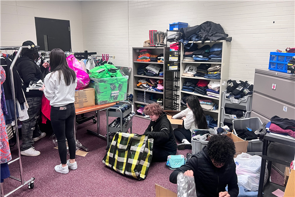 D214 students organize donated clothing items in the "clothing closet" for families in need. They also run a food pantry as a service project for their sociology class.