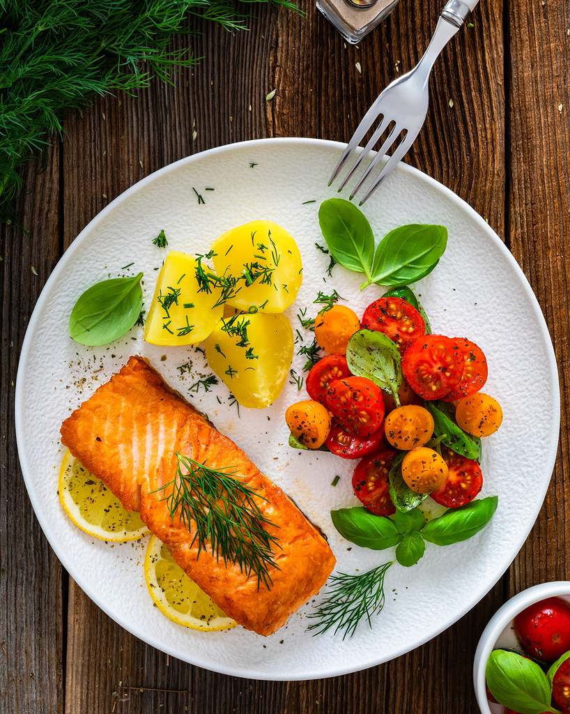 White plate with salmon, tomatoes and vegetables with a fork