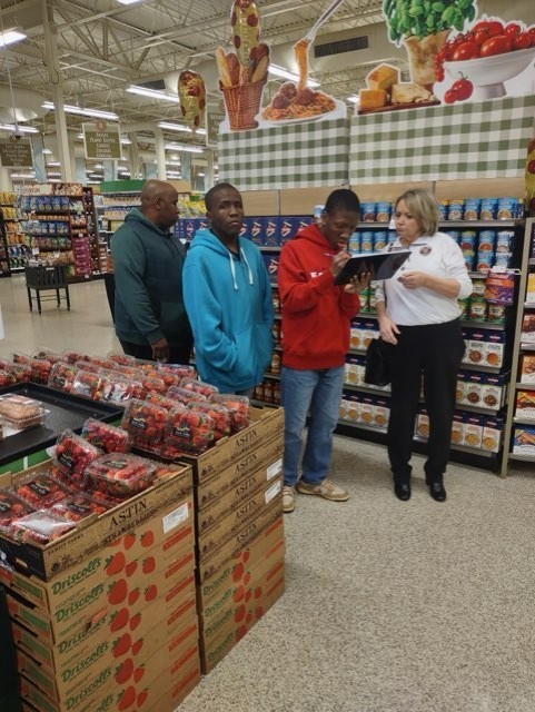four people looking at a list in a store with produce