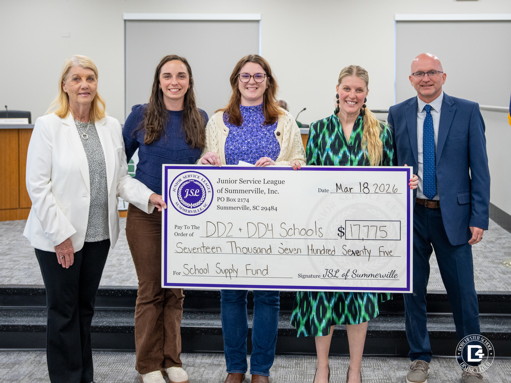 Five adults stand in a school board room holding a large ceremonial check from the Junior Service League of Summerville for $17,775 made out to DD2 and DD4 Schools for a school supply fund, dated March 18, 2026, with a Dorchester School District Four logo visible in the bottom corner.