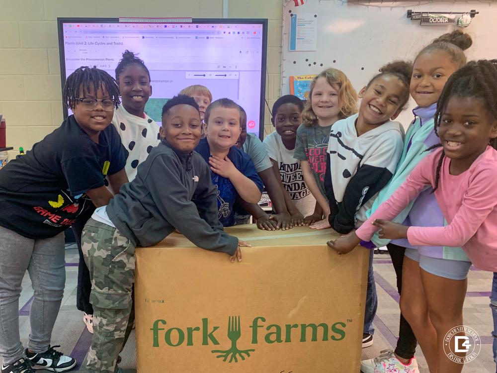 Students standing next to a fork farms box