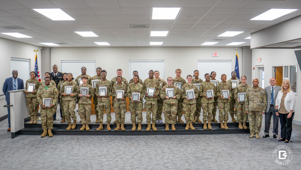 Woodland High School JROTC cadets stand with their wooden plaques on the board room steps alongside Principal Michael White, JROTC instructors, Superintendent Jeffrey Beckwith, and Board Chair Phyllis Hughes.