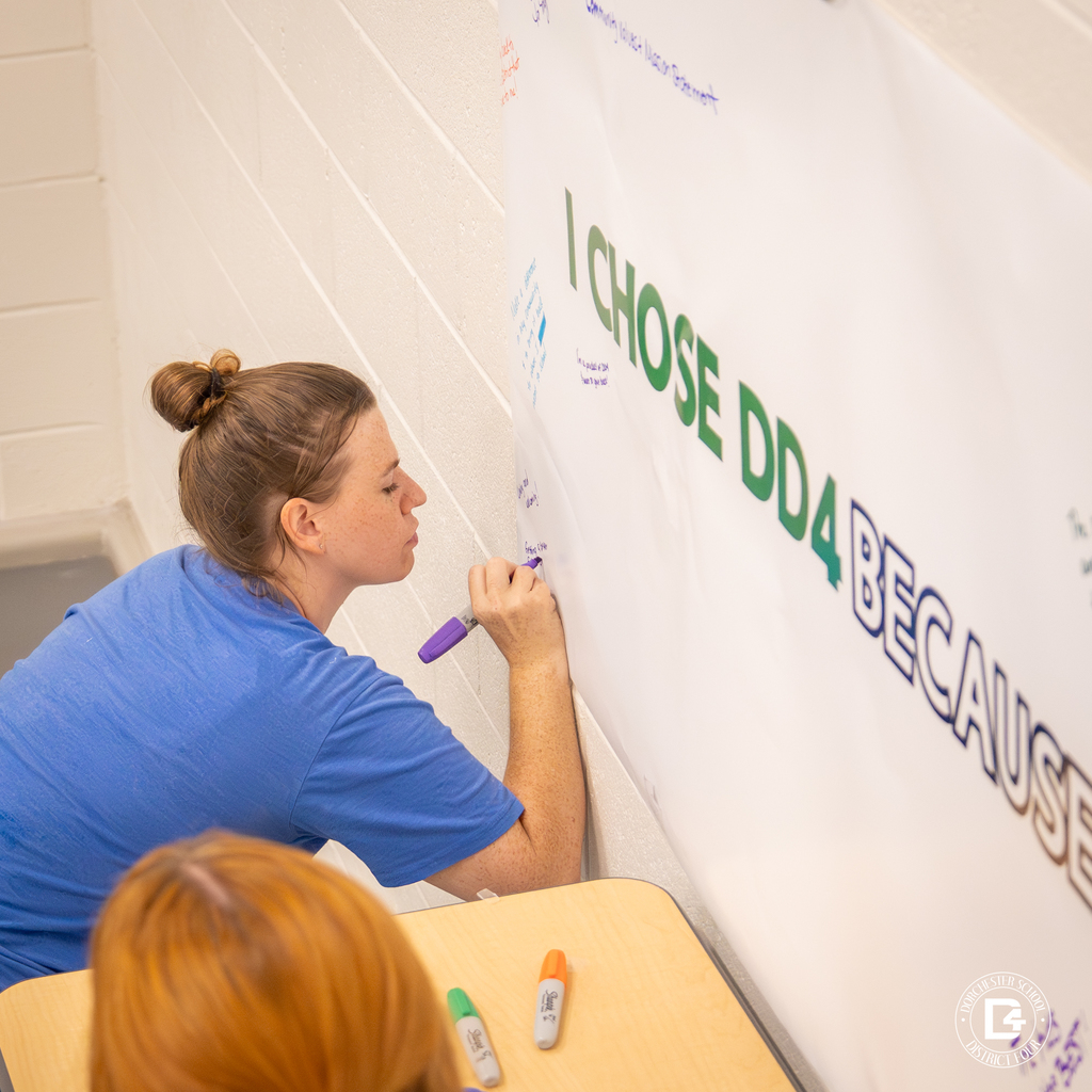 A new employee writes on a large poster that reads “I CHOSE DD4 BECAUSE” as part of a welcome activity.