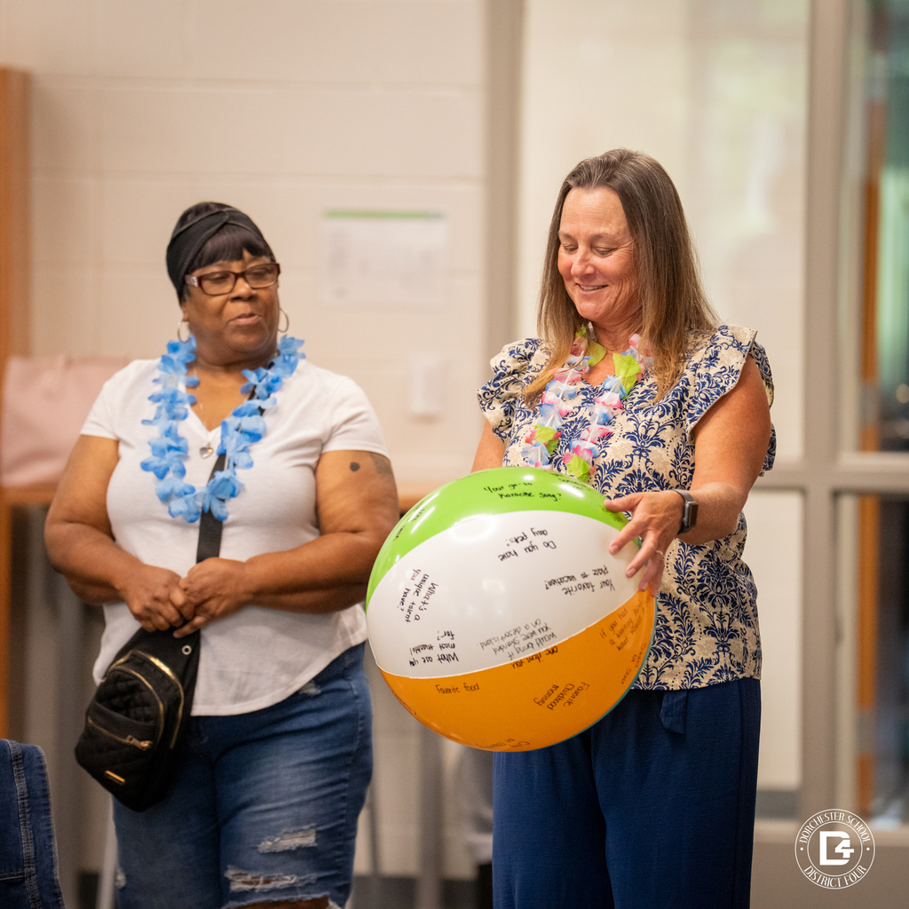 Two women wearing leis participate in an icebreaker activity with a question-covered beach ball.