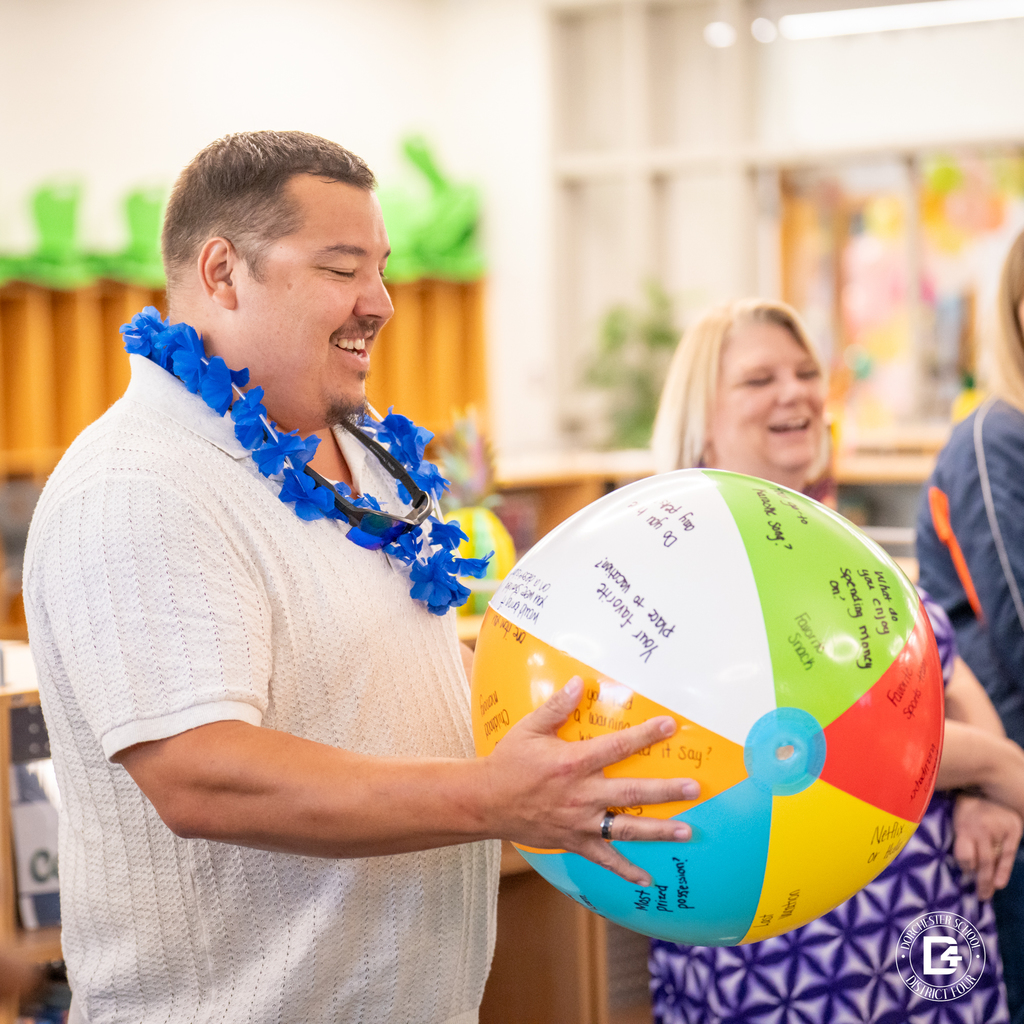 A man wearing a blue lei smiles while holding a colorful question ball during the Luau-themed orientation.
