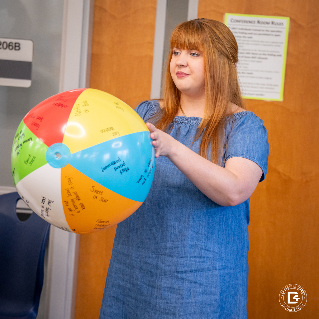 A woman in a denim dress holds a colorful beach ball covered in questions for an introduction activity.