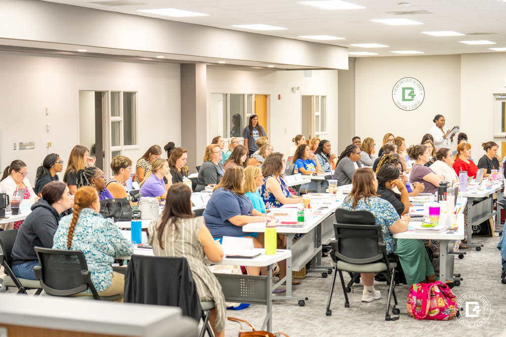 Alternate angle of the training room showing a large group of teachers participating in the session, seated at tables with materials, water bottles, and laptops.