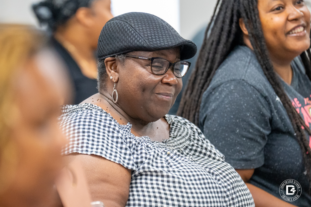 A woman in a checkered top and black cap smiles warmly during the in-service session, with another driver beside her smiling in a graphic t-shirt.