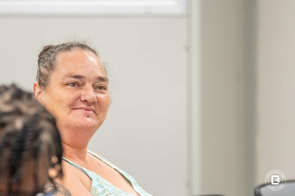 A woman with a nose ring and tattoo smiles slightly while seated in the meeting room.