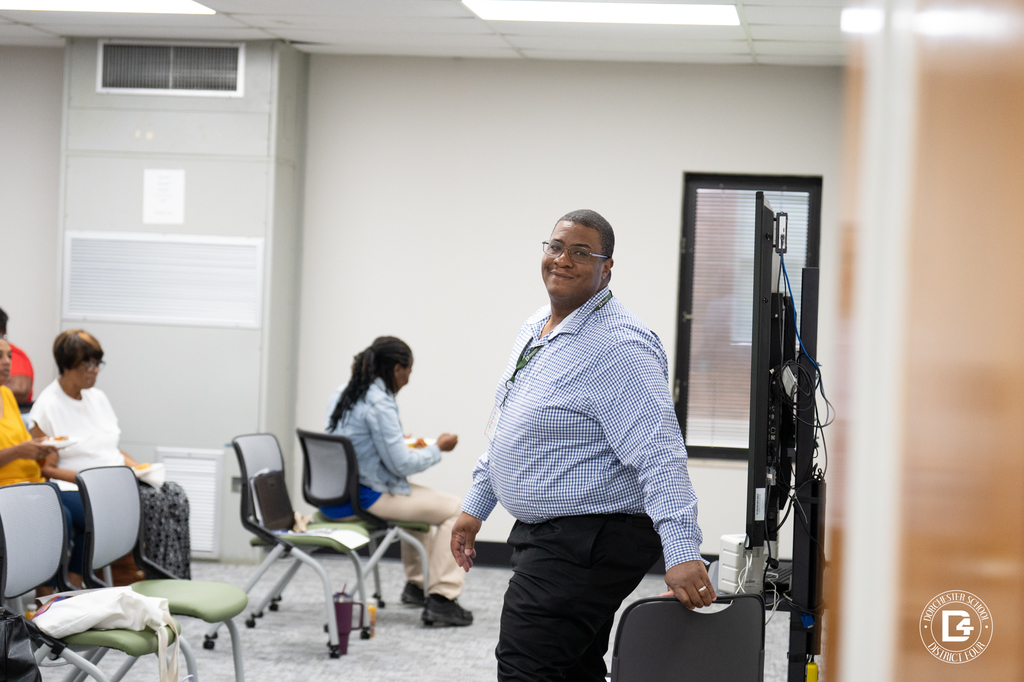 A man in a checkered shirt smiles at the camera while standing near a row of chairs in the training room.