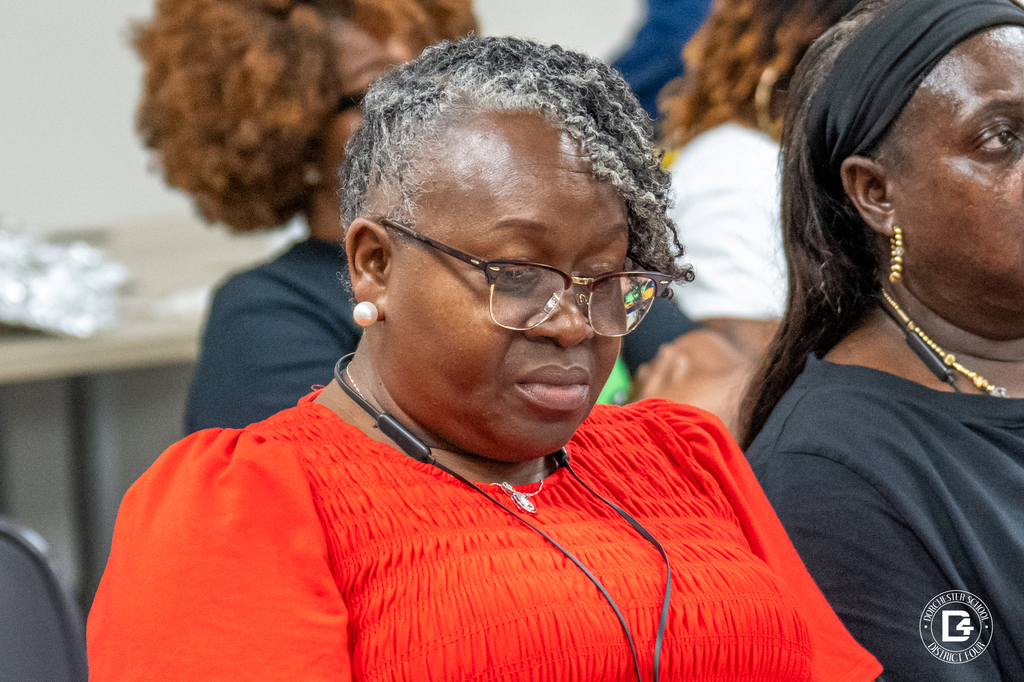 A woman in a red top reads attentively during the training, wearing glasses and a headset.