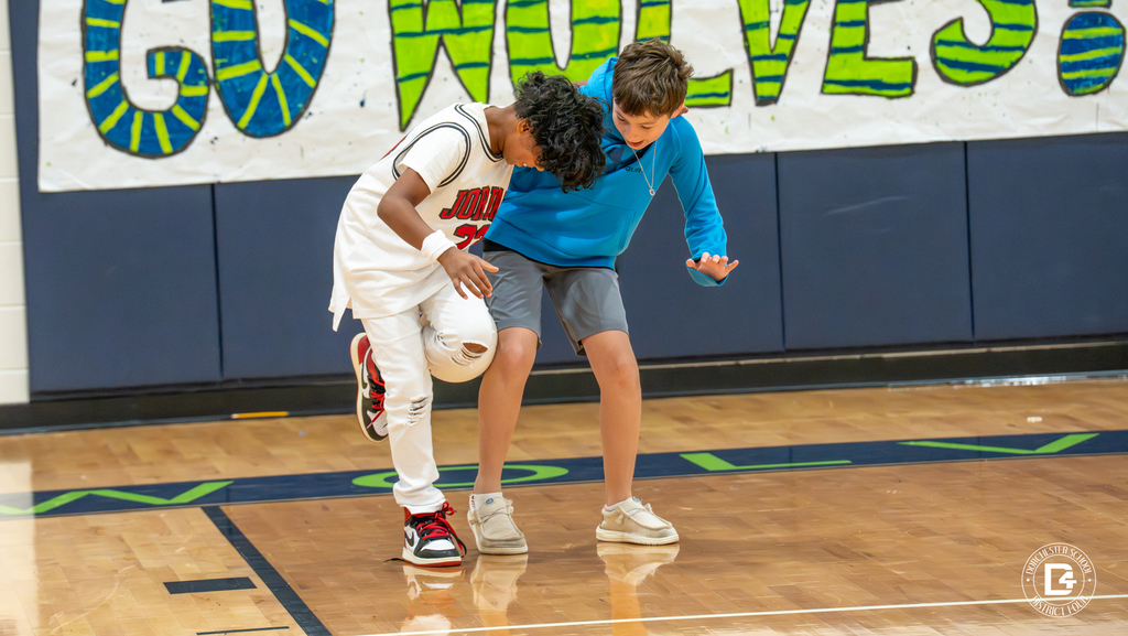 Two boys, arms linked, work together in a three-legged race on the gym floor during the pep rally.