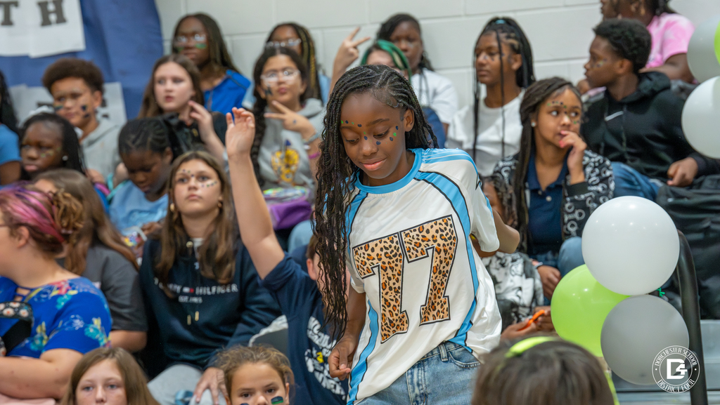 A girl with face paint wearing a sports jersey decorated with “77” walks through the crowd of students in the bleachers during the pep rally.
