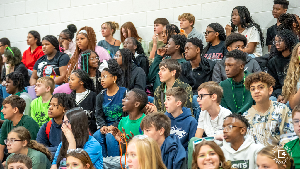 A section of bleachers full of middle school students, many dressed in school colors, watching the pep rally with excitement.