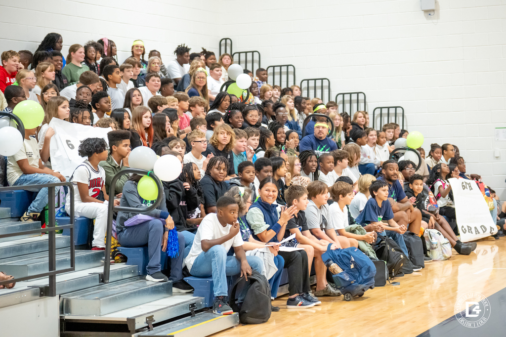 A crowded gym bleacher filled with Woodland Middle School students cheering, clapping, and smiling during the pep rally.
