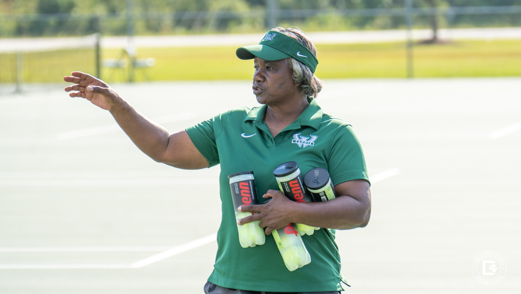 The Woodland High School girls’ tennis coach, in a green visor and shirt, gives instructions while holding several containers of tennis balls.