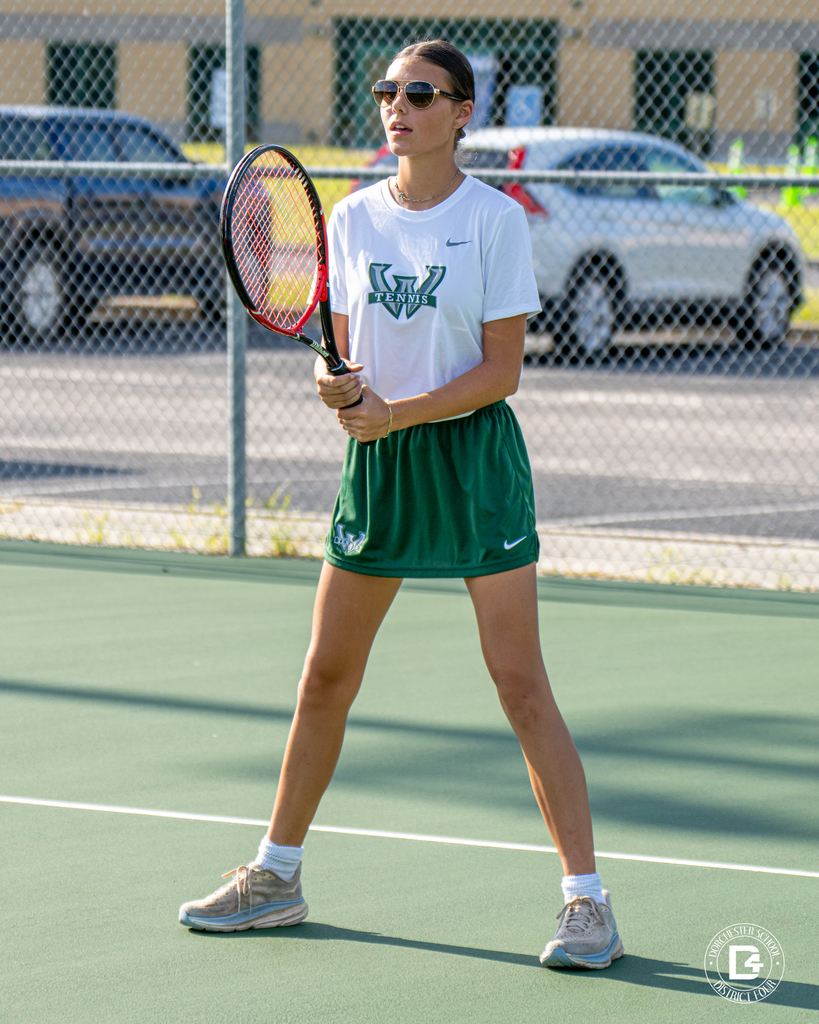A Woodland High School tennis player wearing sunglasses stands on the court, holding her racket ready in both hands.