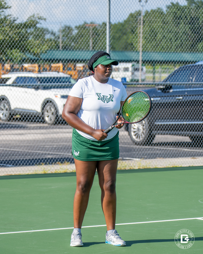 A Woodland High School tennis player stands in position on the court, holding her racket and watching the play.