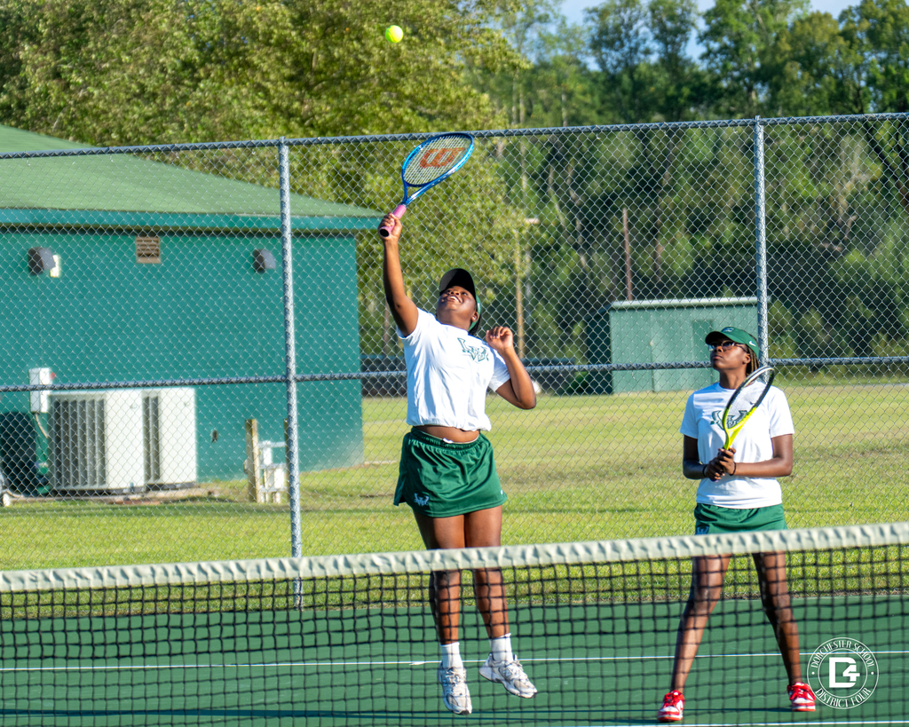 Two Woodland High School doubles partners play at the net; one jumps to make a shot while the other prepares with her racket.
