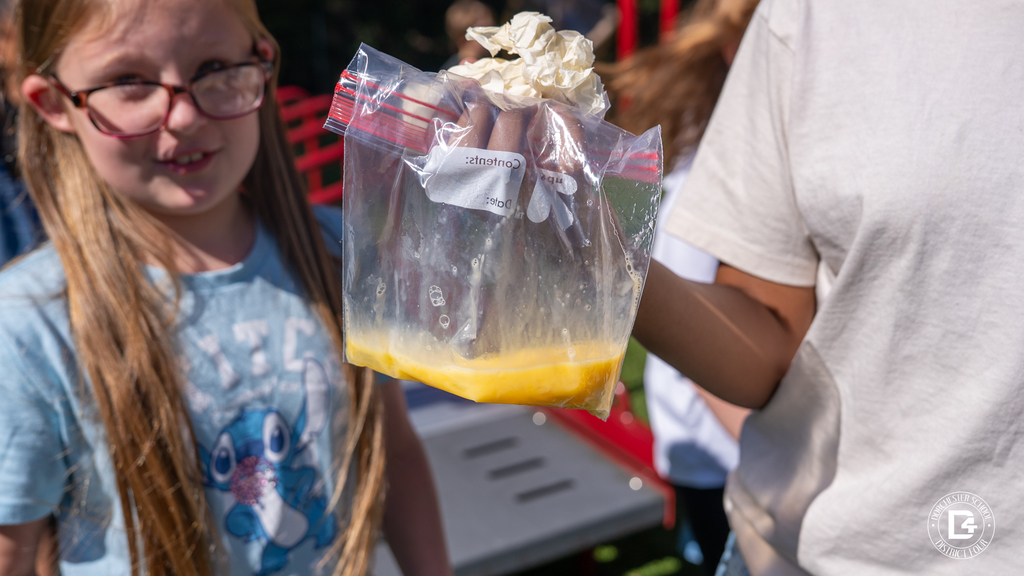 A student holds a clear plastic bag filled with scrambled egg remains, showing one of the failed egg drop attempts.