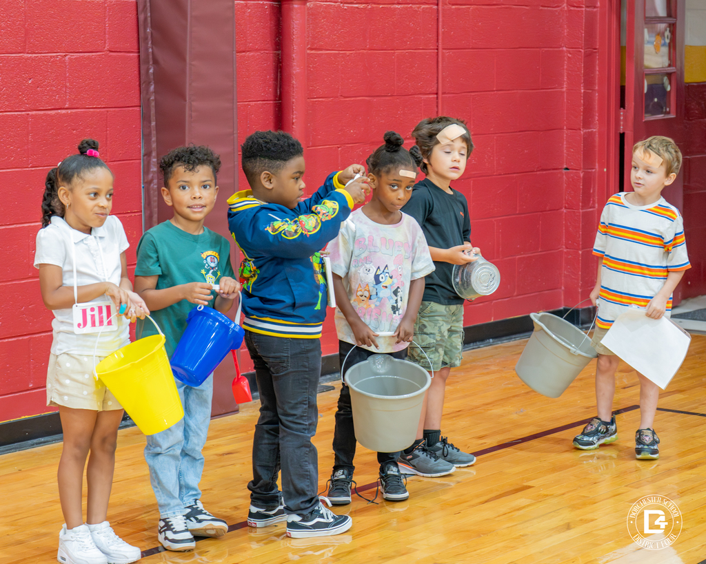 A group of children dressed as Jack and Jill hold colorful buckets and props while standing in a line.