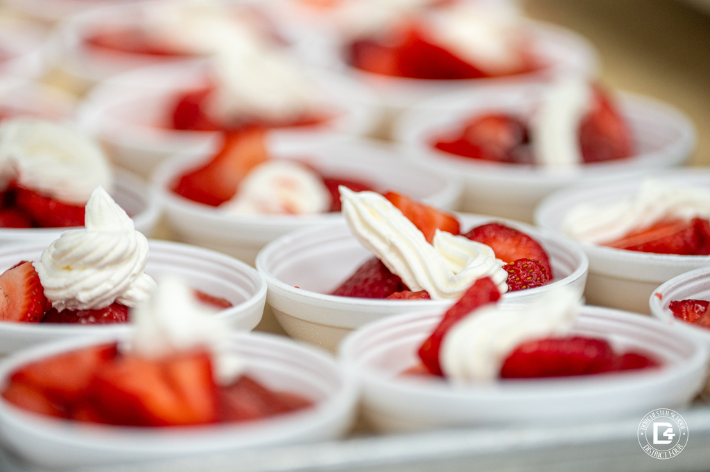 Close-up of dessert cups filled with strawberries and topped with swirls of whipped cream, arranged in neat rows.