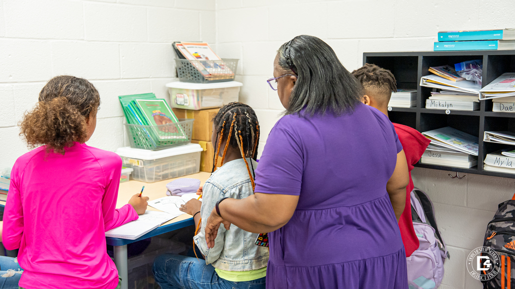 4th-grade teacher Patrice Anderson stands beside a small group of students working at a table. She observes closely as students write in their notebooks during a compare-and-contrast lesson at Harleyville Elementary School.
