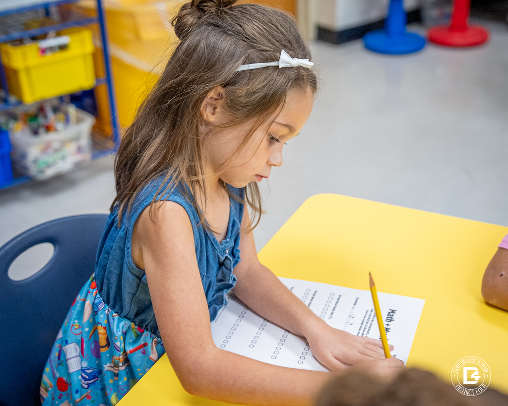A student wearing a blue dress writes on her Math + Music Challenge worksheet, focused on grouping beats into patterns.